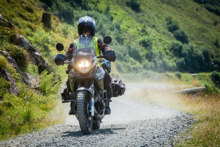 Motorcyclist travels on gravel road through lush green landscape, capturing the thrill of adventure.